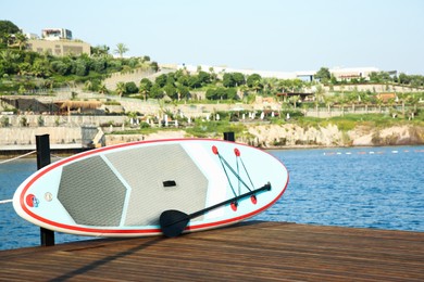 Photo of SUP board with paddle on wooden pier near sea