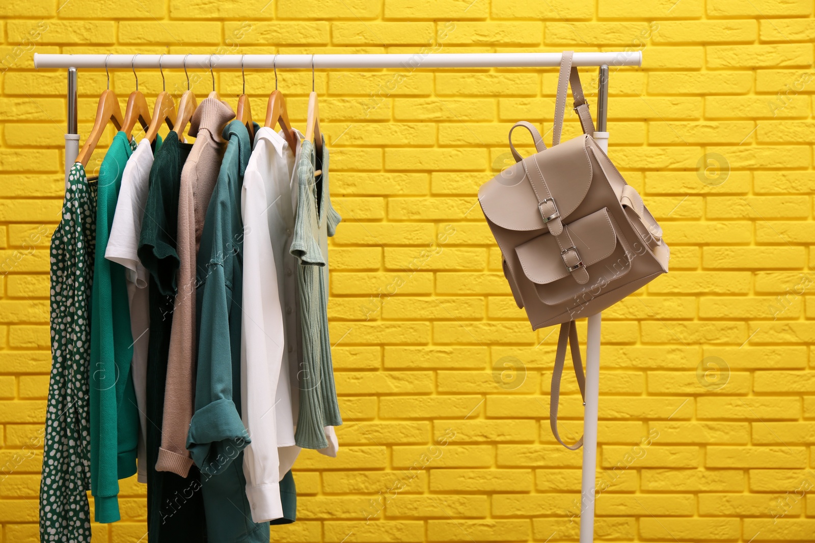 Photo of Rack with different stylish clothes and backpack near yellow brick wall