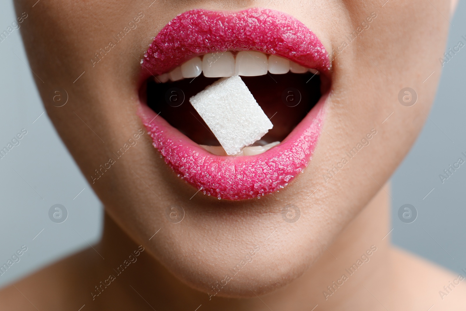 Photo of Woman with beautiful lips eating sugar cube on light grey background, closeup