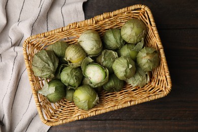 Photo of Fresh green tomatillos with husk in wicker basket on wooden table, top view