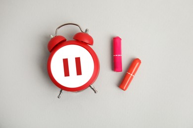 Image of Menopause. Alarm clock with pause symbol and tampons on light grey background, flat lay