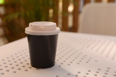 Takeaway paper cup with plastic lid on white table indoors, space for text