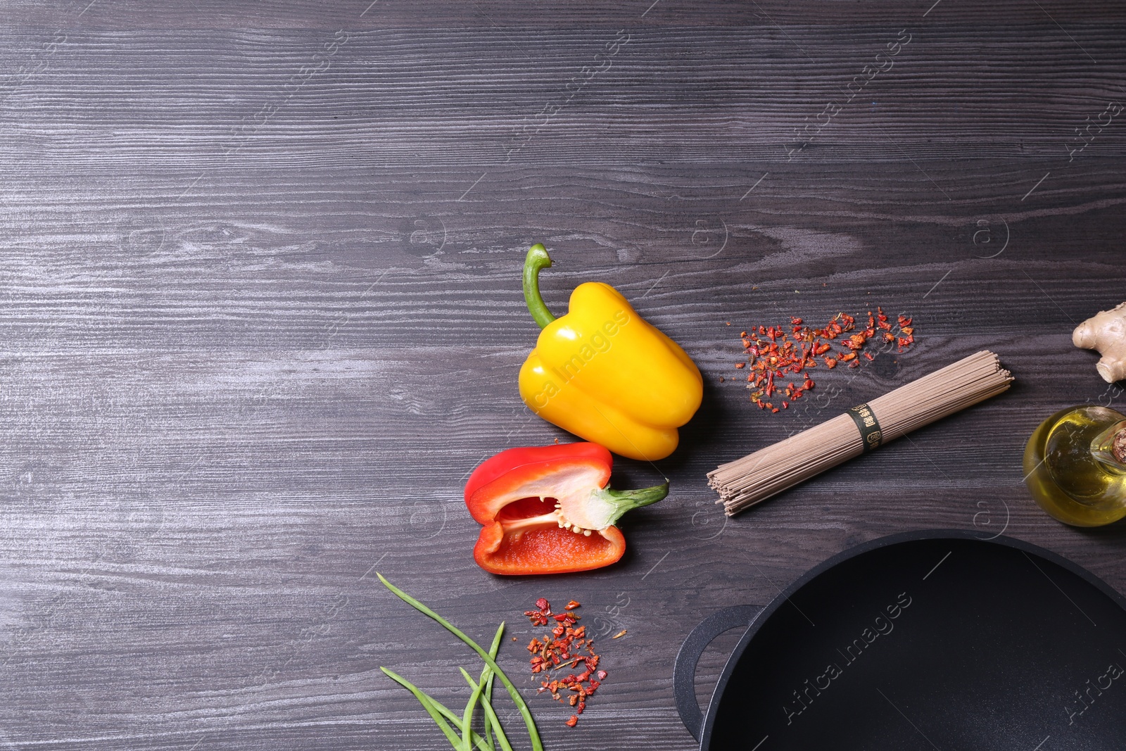 Photo of Empty iron wok and ingredients on dark grey wooden table, flat lay. Space for text