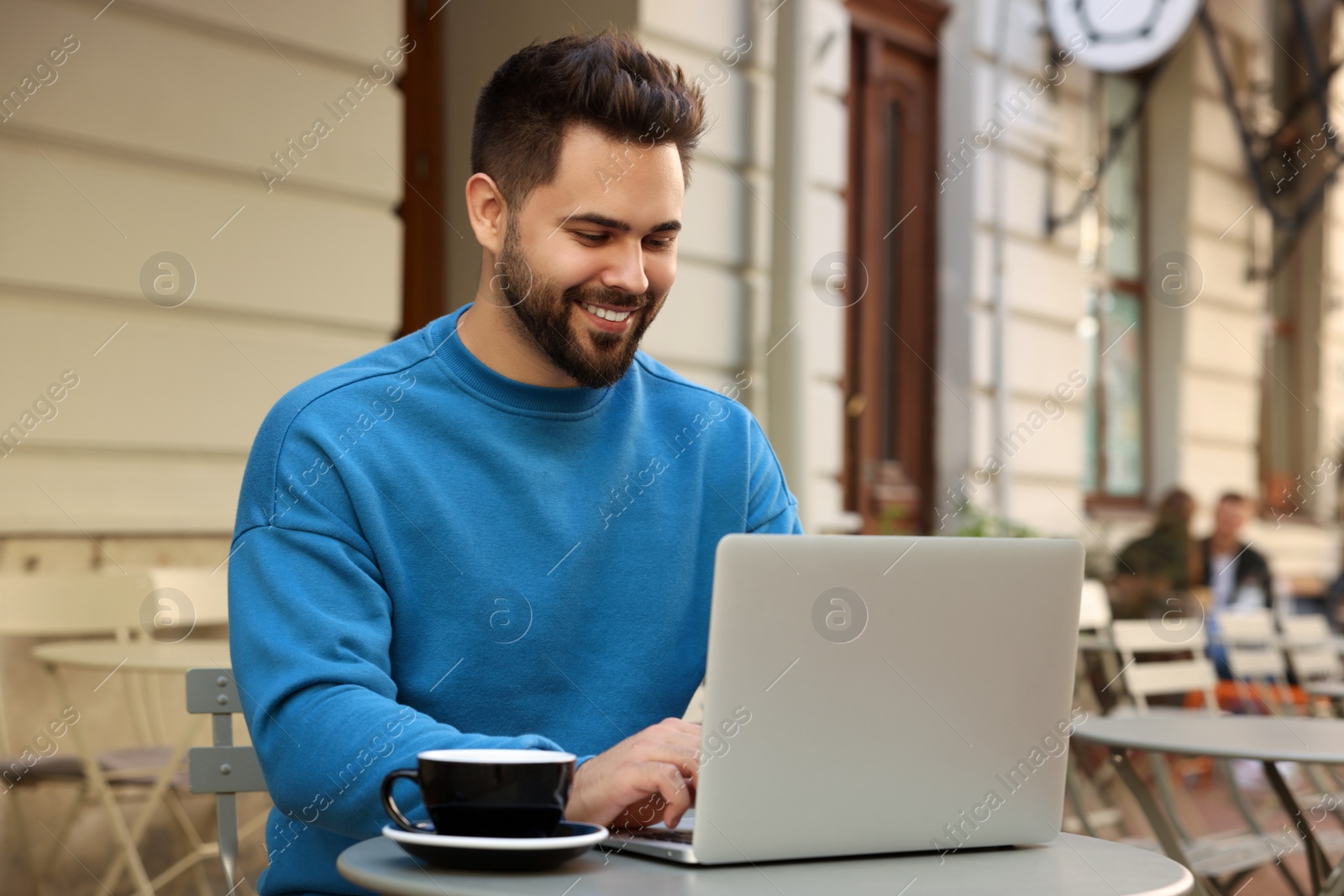 Photo of Handsome young man working on laptop at table in outdoor cafe