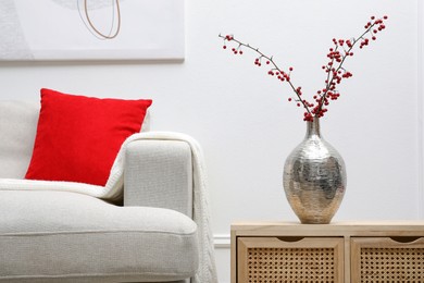 Photo of Hawthorn branches with red berries on wooden commode in living room