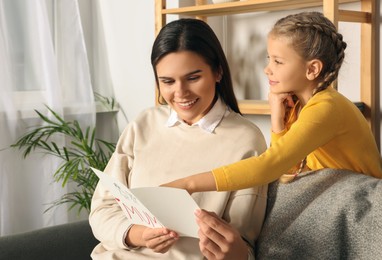 Photo of Happy woman receiving greeting card from her little daughter at home