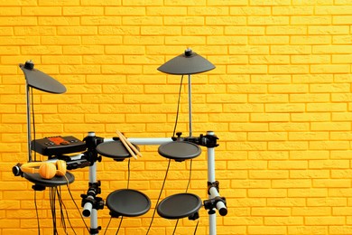 Photo of Modern electronic drum kit near yellow brick wall indoors, space for text. Musical instrument