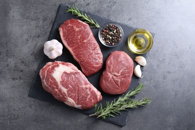 Photo of Raw beef steaks, oil and spices on grey background, top view