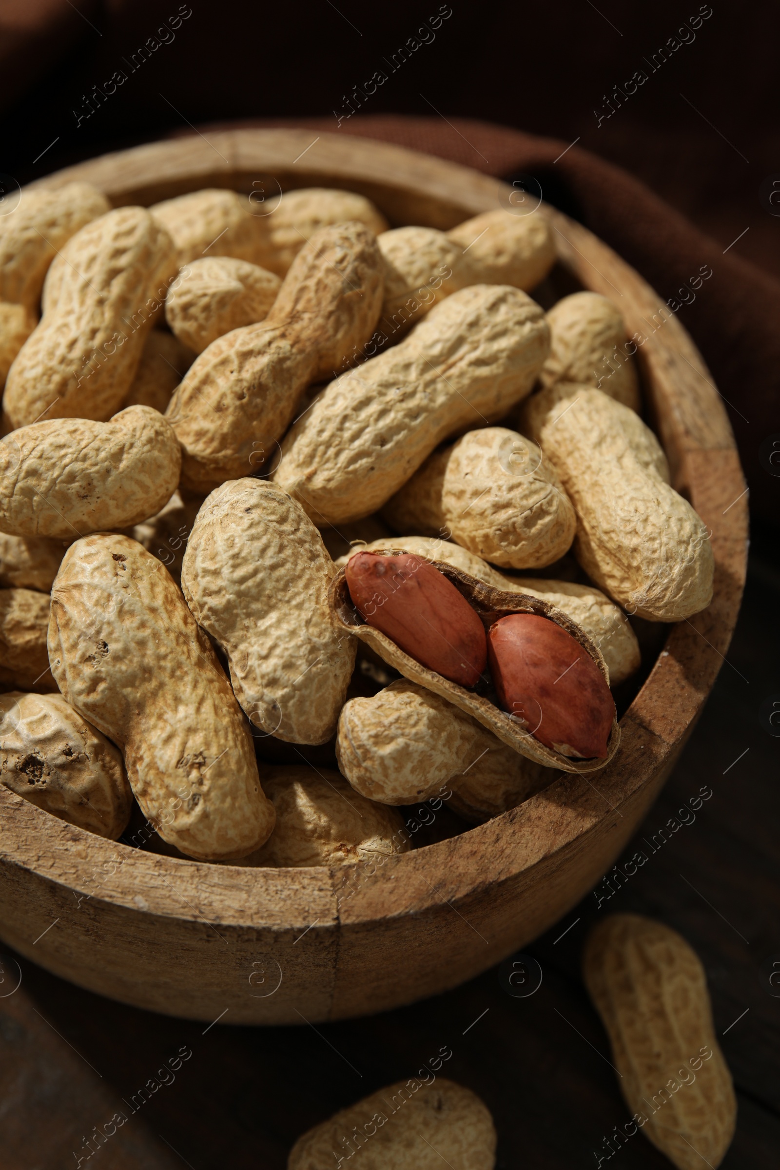 Photo of Fresh unpeeled peanuts in bowl on wooden table, closeup