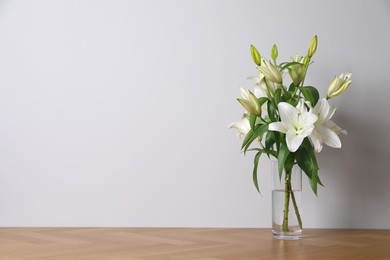 Photo of Beautiful bouquet of lily flowers in glass vase on floor near white wall. Space for text