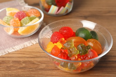 Different delicious gummy candies in glass bowl on wooden table