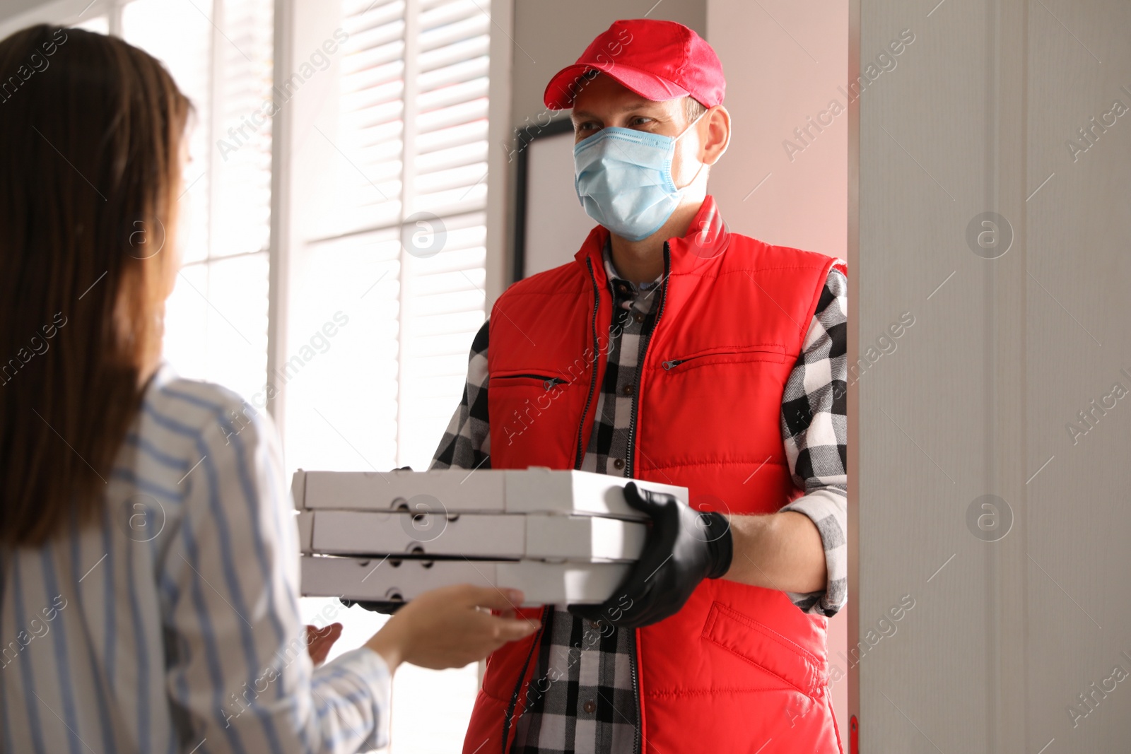 Photo of Courier giving pizzas to woman indoors. Food delivery service during coronavirus quarantine