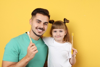 Little girl and her father with toothbrushes on color background. Teeth care