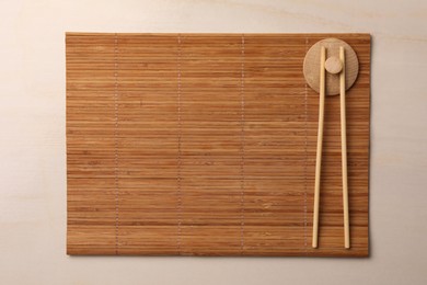 Photo of Bamboo mat and chopsticks on beige table, top view. Space for text