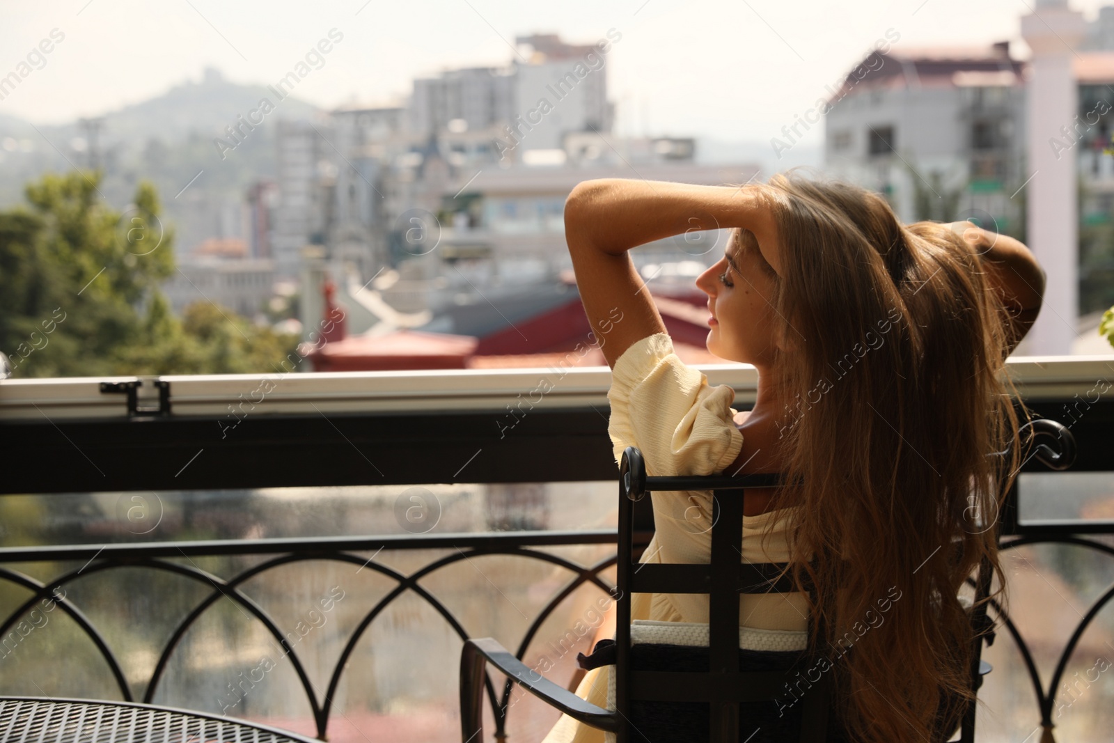 Photo of Beautiful young woman sitting on balcony, back view. Space for text