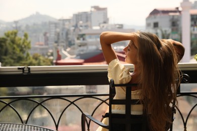 Beautiful young woman sitting on balcony, back view. Space for text