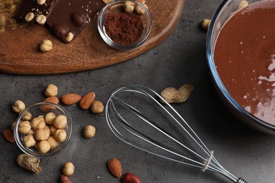 Bowl of chocolate cream, whisk, and nuts on gray table, flat lay