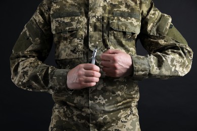 Photo of Soldier pulling safety pin out of hand grenade on black background, closeup. Military service