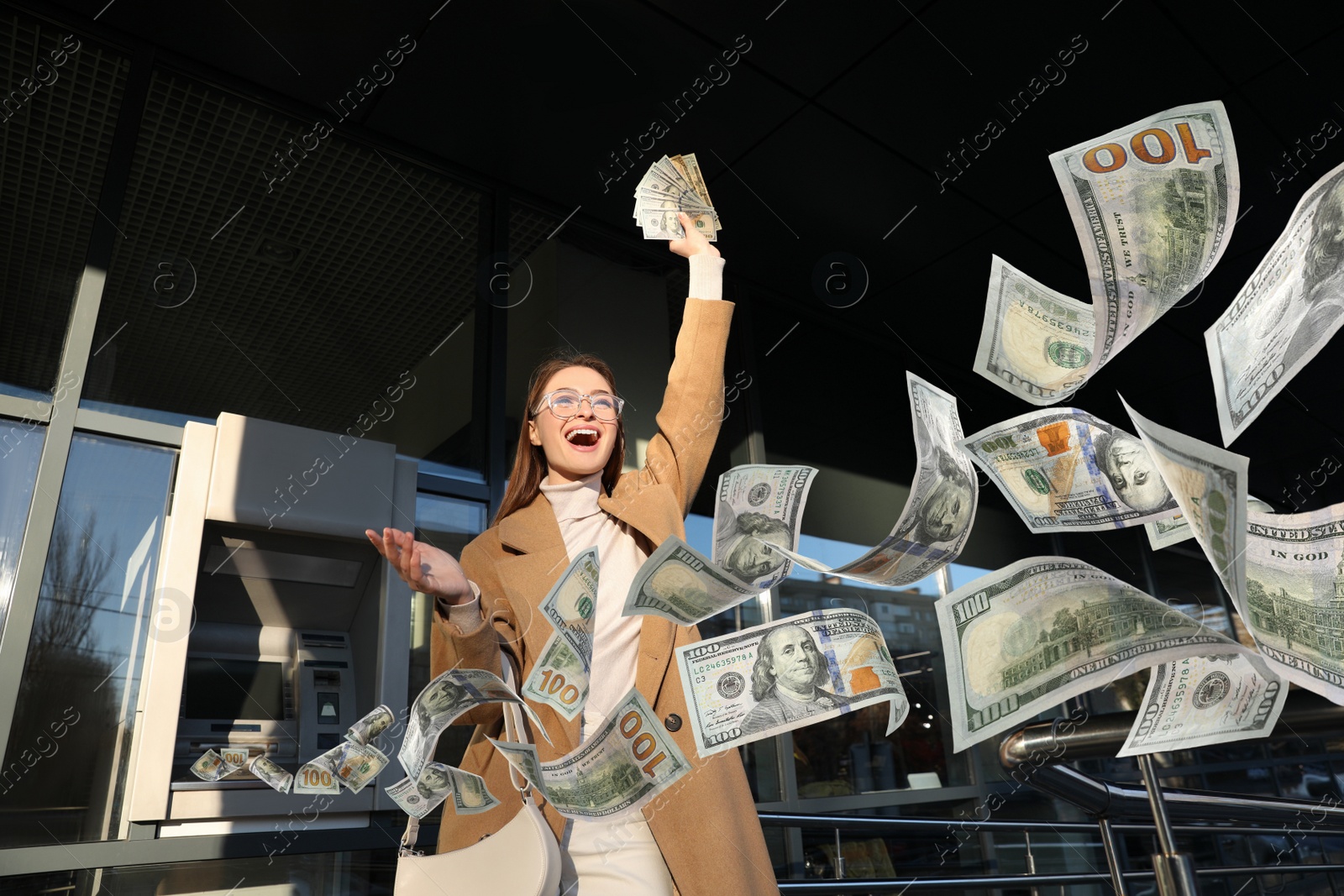 Image of Excited young woman with money near cash machine outdoors