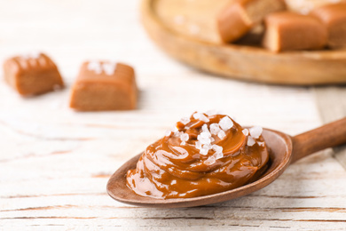 Photo of Salted caramel in spoon on white wooden table, closeup