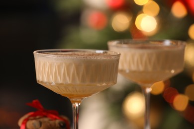 Photo of Tasty eggnog and cookies against blurred festive lights, closeup