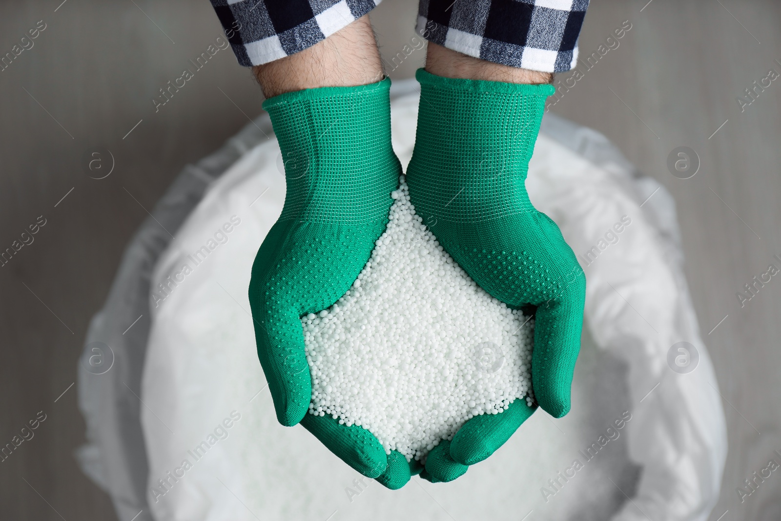 Photo of Farmer holding pile of ammonium nitrate pellets over bag, top view. Mineral fertilizer