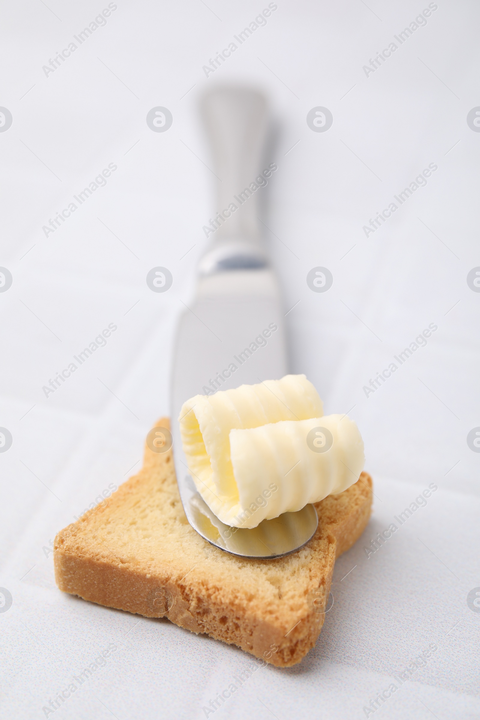 Photo of Tasty butter curl, knife and piece of dry bread on white tiled table, closeup