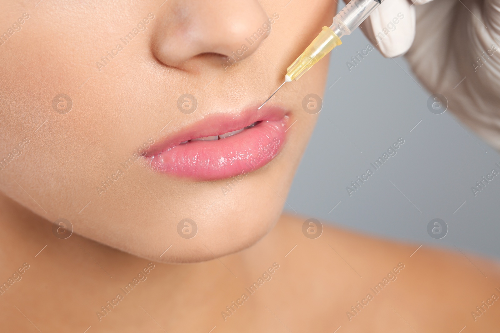 Photo of Young woman getting lips injection on grey background, closeup. Cosmetic surgery