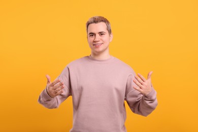 Photo of Happy man inviting to come in on orange background