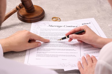 Man and woman signing marriage contract at light grey table, closeup