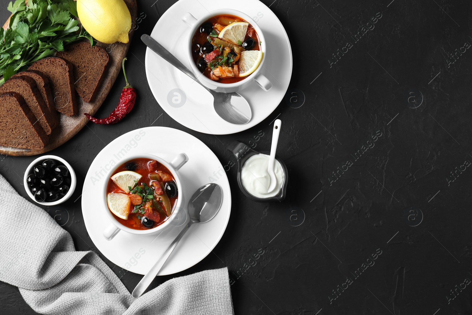 Photo of Meat solyanka soup with sausages, olives and vegetables served on dark grey textured table, flat lay. Space for text