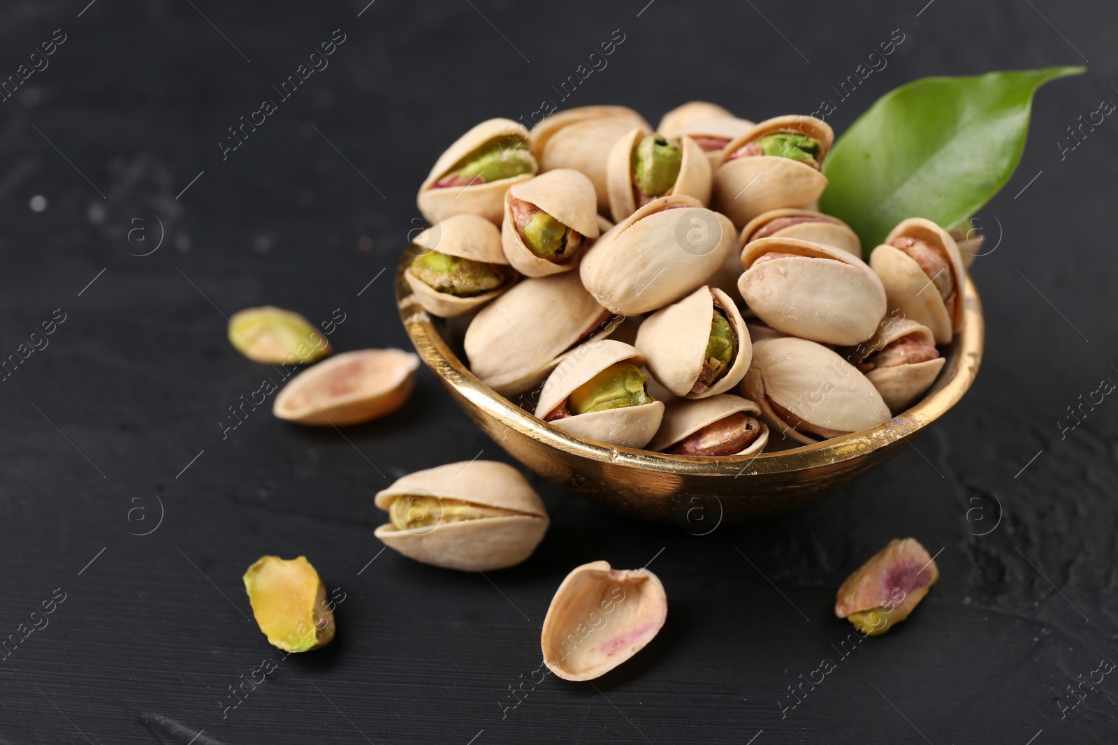 Photo of Tasty pistachios in bowl on black table, closeup. Space for text