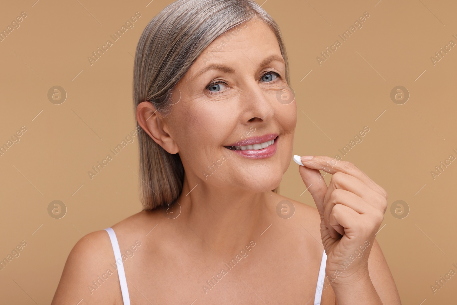 Photo of Beautiful woman taking vitamin pill on beige background