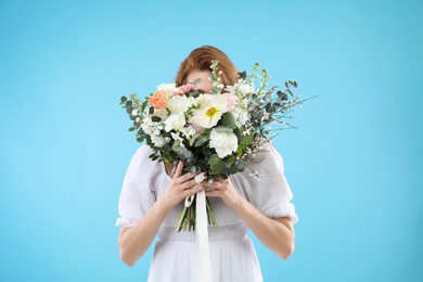 Photo of Woman covering her face with bouquet of beautiful flowers on light blue background