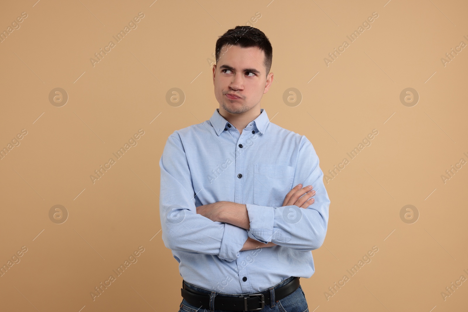 Photo of Resentful man with crossed arms on beige background