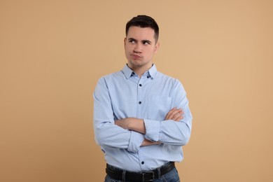 Resentful man with crossed arms on beige background