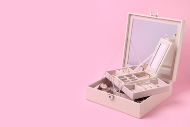 Jewelry box with many different accessories on pink background. Space for text