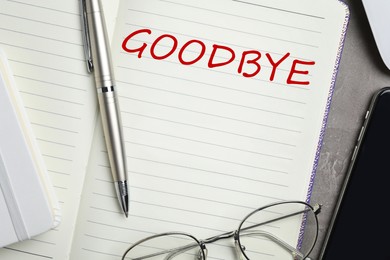 Image of Notebook with word Goodbye, pen and glasses on table, closeup