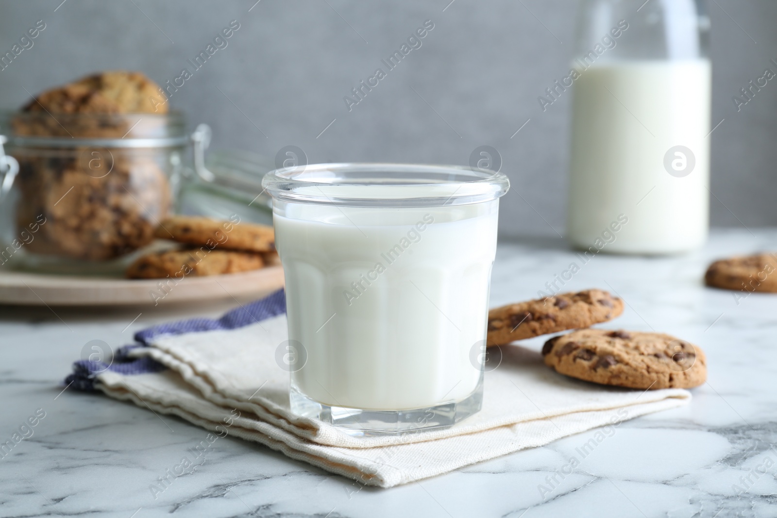 Photo of Tasty chocolate chip cookies and glass of milk on white marble table