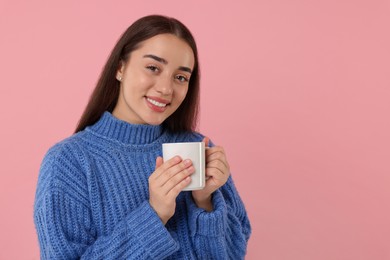 Photo of Happy young woman holding white ceramic mug on pink background, space for text