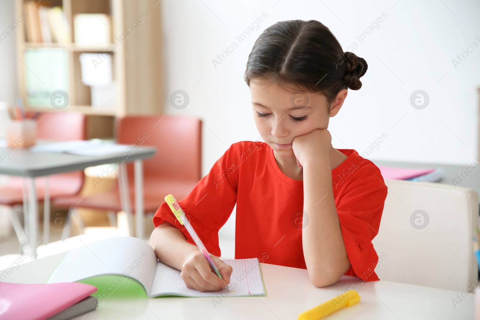 Photo of Cute little child doing assignment at desk in classroom. Elementary school