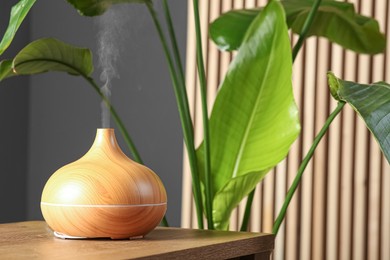 Photo of Air humidifier on wooden table near green houseplant indoors. Space for text