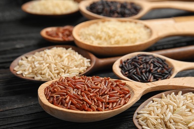 Photo of Spoons with different types of rice on wooden background, closeup