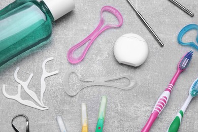 Photo of Tongue cleaners and other oral care products on grey table, flat lay