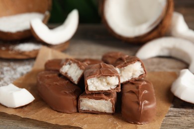 Delicious milk chocolate candy bars with coconut filling on wooden table, closeup. Space for text