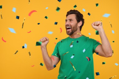 Happy man under falling confetti on orange background