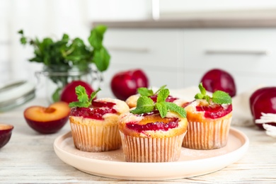 Delicious cupcakes with plums on white wooden table