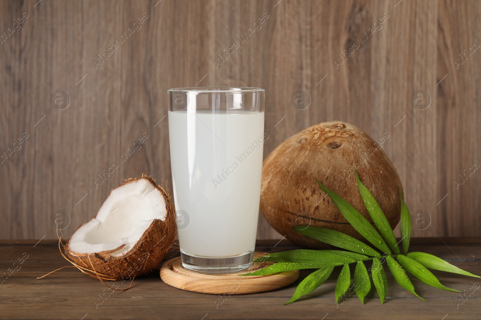 Photo of Glass of coconut water, leaf and nuts on wooden table