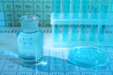 Laboratory glassware and petri dish on periodic table of elements, closeup. Color tone effect