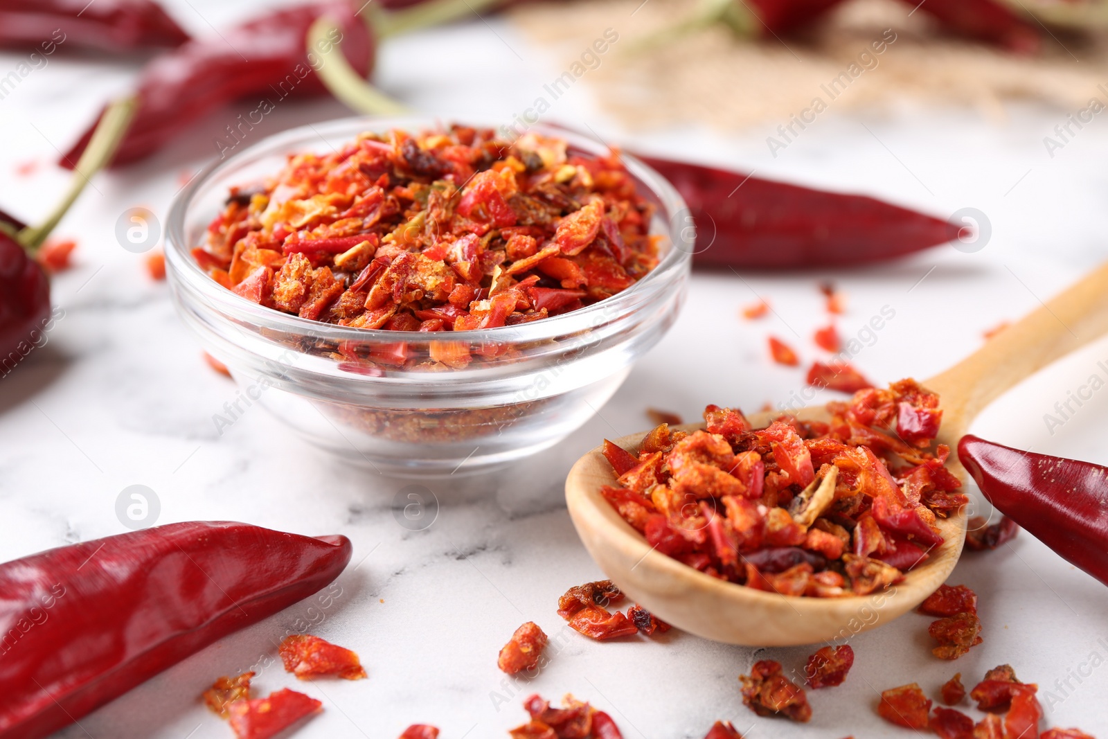 Photo of Chili pepper flakes and pods on white marble table, closeup